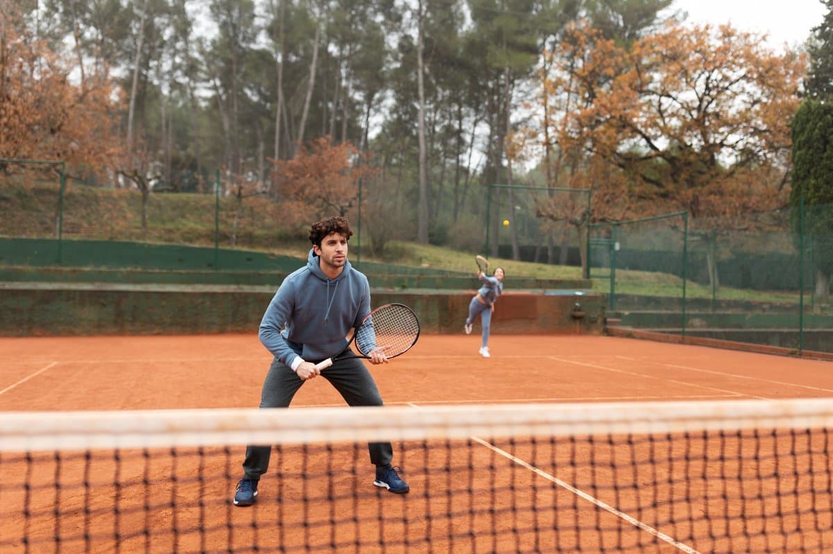 Dua orang berlatih bermain tenis di lapangan tanah liat